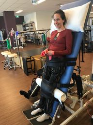 A young woman, Ebonny, stands upright in hospital as she's attached to a recovery bed following rehabilitation as a result of a catastrophic injury. She's wearing a red top, black trousers and smiles at the camera.
